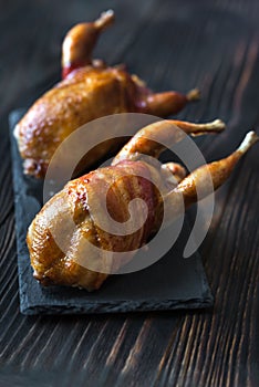 Two baked quails wrapped in bacon on the black stone board