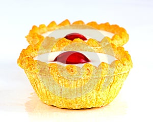 Two Bakewell Tarts with white icing and a red cherry.