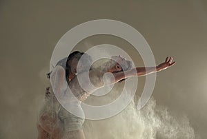 Two ballet dancers dance against white flour cloud in air