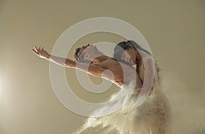 Two ballet dancers dance against white flour cloud in air