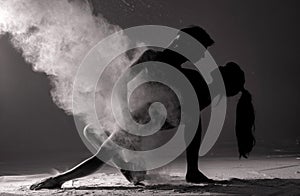 Two ballet dancers perform dance against background of white flour cloud in air