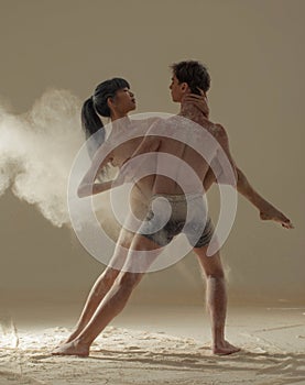 Two ballet dancers perform dance against background of white flour cloud in air