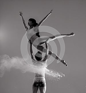 Two ballet dancers perform dance against background of white flour cloud in air