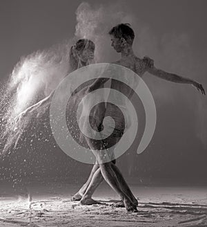 Two ballet dancers perform dance against background of white flour cloud in air