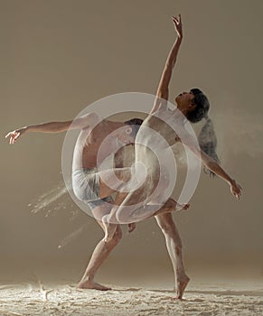 Two ballet dancers perform dance against background of white flour cloud in air