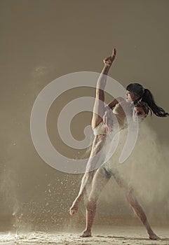 Two ballet dancers perform dance against background of white flour cloud in air