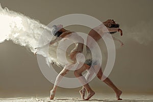 Two ballet dancers perform dance against background of white flour cloud in air