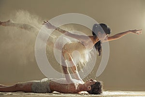 Two ballet dancers perform dance against background of white flour cloud in air