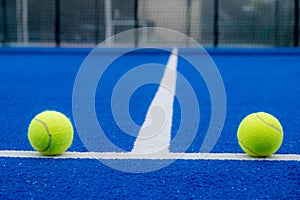 two balls on the baseline of a blue paddle tennis court