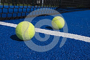 Two balls near the net of a paddle tennis court