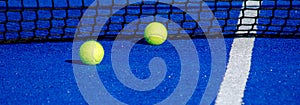 Two balls by the net of a paddle tennis court