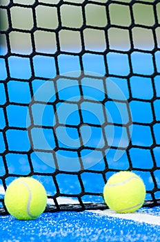 two balls next to the net of a paddle tennis court