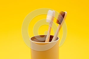 Two bamboo toothbrushes in glass on yellow background