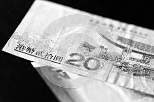 Two banknotes of twenty Hong Kong dollars on a dark background. Black and white