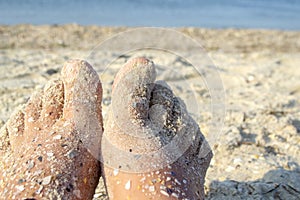 Two bare feet of caucasian woman soiled in sand with shell rock on sandy sea