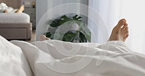 Two bare feet of man lie under blanket and reflect in wardrobe mirror. Male