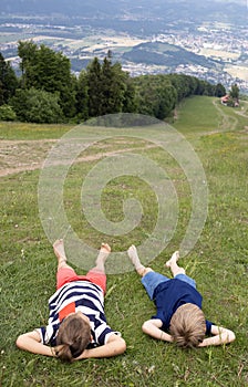 Two barefoot boy friends lie on a mountainside on a summer day, relax, enjoy the scenery