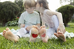 two barefoot children. a boy and a girl, 7-8 years old, sitting on the grass, red hearts drawn on their feet