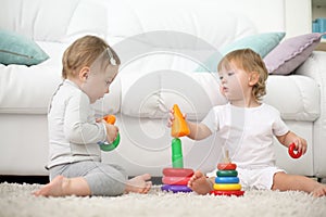 Two barefoot kids sit on carpet and play with