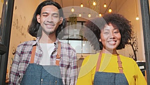 Two baristas at a cafe door, arms crossed, look at a camera with welcome smile.