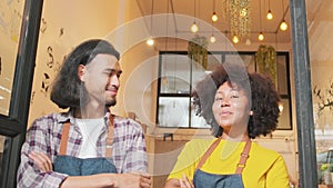 Two baristas at a cafe door, arms crossed, teasing together with a happy smile.