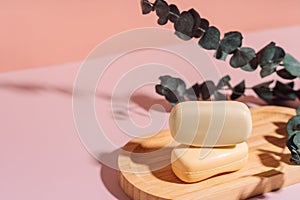 Two bars of soap in a wooden soap dish with dried flowers against a pink background