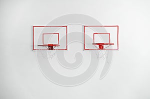 Two basketball backboards with red metal hoops on white concrete wall