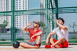 Two basketball players having some rest sitting on the court after an exhausting basketball game