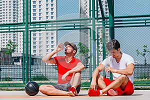 Two basketball players having some rest sitting on the court after an exhausting basketball game