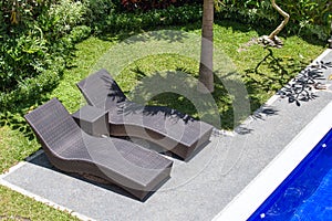 Two beach chairs next to a swimming pool in a tropical garden.