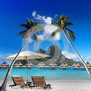 Two beach chairs and solar umbrella under a palm tree and a view of the sea and mountains. Tahiti