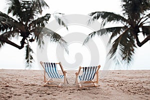 two beach lounge chairs under coconut tree on the beach