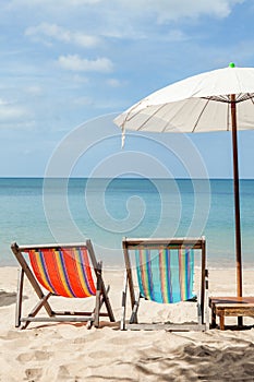 Two beach lounge chairs under umbrella on beach.