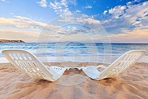 Two beachchairs on the sand near sea and colorful sky