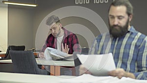 Two bearded office workers work in the office studying the reporting documentation. Colleagues read papers with work