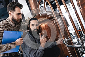 Two bearded professional brewers inspect equipment for making crafted beer.