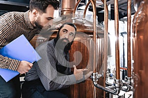 Two bearded professional brewers inspect equipment for making crafted beer.