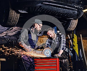 Two b mechanics working with an angle grinder in a garage.