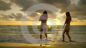 Two beautiful Asian women are having fun dancing on the beach at sunset on vacation, freedom concept, tourism, adventure, carefree