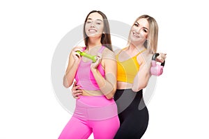 Two beautiful, athletic, slender and cheerful female friends are smiling and holding dumbbells and a kettlebell in their