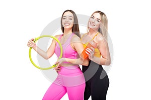 Two beautiful, athletic, slim and cheerful female friends are smiling and holding a hoop and a bottle of water in their