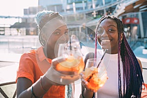 Two beautiful black women sisters sitting bar making a toast smiling