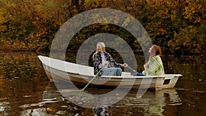 Two beautiful blond and ginger women sits in a boat on a lake in a fairy autumn forest