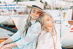 Two beautiful blonde girls friends mother and daughter in white and straw hats on the yacht at pier