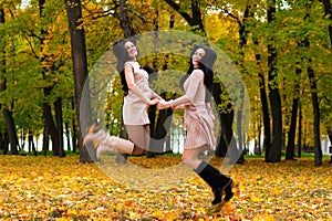 Two beautiful brunette girls jumping on background autumn park