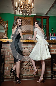 Two beautiful brunette ladies in elegant black and white lace dresses posing in vintage scenery