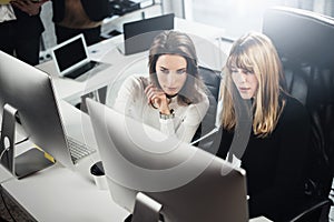 Two beautiful business woman working at modern lightfil office.Handsome girls at working process on desk top computer