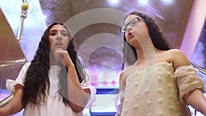 Two beautiful cheerful girls go down the escalator during shopping and discuss shopping in the mall with a good mood. HD