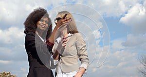 Two beautiful cheerful mixed race businesswomen in suits are smiling and happily talking. The caucasian one is showing