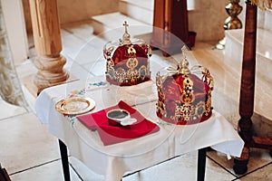 Two beautiful crowns with gold and red cloth stand on a table in the church before the baptism of the baby